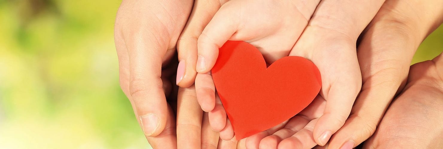 Red heart in family hands on bright background